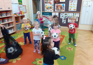 Dzieci w rozsypce stoją na dywanie i trzymają piłki w rękach