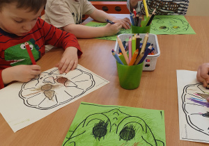 Dzieci przy stoliku kolorują maski dinozaura.