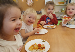 Dzieci siedzą przy stole i jedzą pizzę w radosnym nastroju.