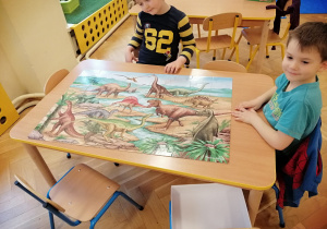 Chłopcy układają puzzle z dinozaurami.