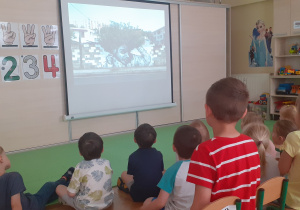 Dzieci słuchają i oglądają prezentacje multimedialną na temat tworzenia murali