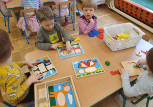 Dzieci przy stoliku bawią się układankami z figurami