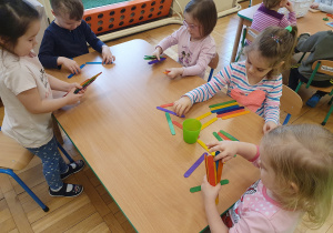 Dzieci przy stoliku układają różne formy z kolorowych patyczków