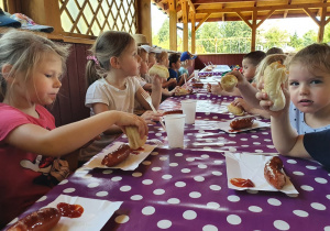 Dzieci przy stoliku jedzą kiełbaskę