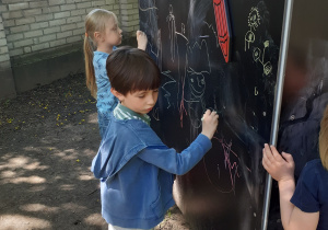 Dzieci rysują kolorową kredą po tablicy