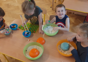 Dzieci siedzą przy stolikach i korzystają z materiałów sensorycznych