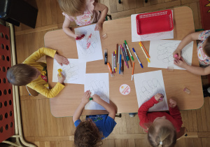 Dzieci siedzą przy stolikach i projektują wzorek na paznokciach,