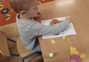 Chłopiec przykleja kolorowe liście.