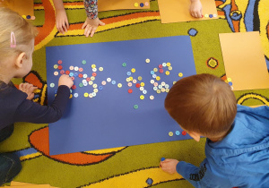 Dzieci bawią się kolorowymi guzikami układając z nich wzory