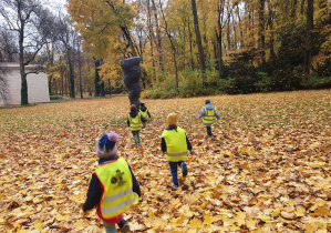Dzieci biegają wśród jesiennych liści.