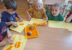 Dzieci za pomocą połówki jabłka namaczanego w farbie robią stempelki dyni