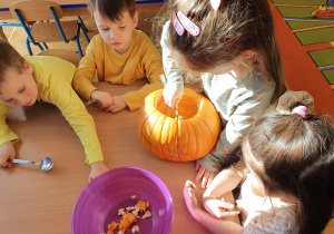 Dzieci za pomocą łyżek wyjmują z dyni nasiona