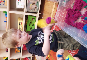 Chłopiec bawi się piaskiem i foremkami.