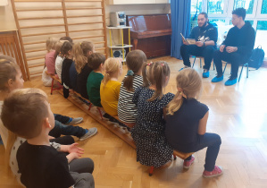Dzieci siedzą na ławeczkach i słuchają opowiadania