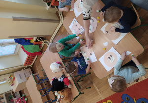 Dzieci przy stoliku wykonują pracę plastyczną.