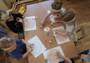 Dzieci przy stoliku wykonują pracę plastyczną.