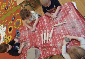 Dzieci przy stolikach bawią się gliną.