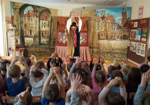 Widownia dzieci naśladuje co robi aktor - podnoszą ręce do góry
