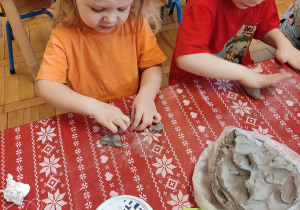 Dziewczynka z chłopcem wyrabia kulki z gliny.