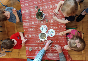 Dzieci siedzą przy stoliku i bawią się gliną.