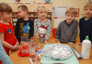 Dzieci stoją przy stoliku wokół przygotowanych materiałów do zajęć