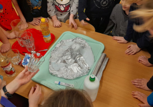 Dzieci przy stoliku obserwują mieszanie składników i reakcje chemiczne