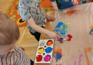 Dzieci malują farbami na folii bąbelkowej.