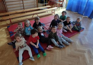 Dzieci siedzą na materacu w sali gimnastycznej.