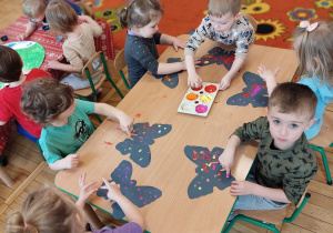 Dzieci siedzą przy stole i wykonują motyle.