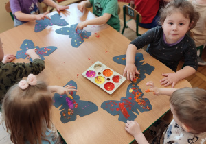 Dzieci siedzą przy stole i malują farbami.