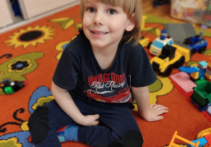 Chłopiec siedzi na dywanie i się uśmiecha.