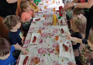 Dzieci jedzą kiełbaskę z grila.