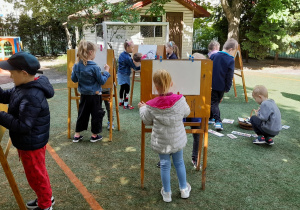 Dzieci stoją przy sztalugach i rysują pastelami