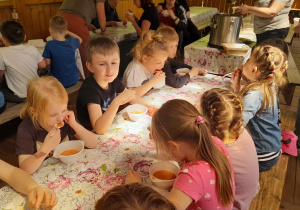 Dzieci siedzą przy stole i jedzą zupę.