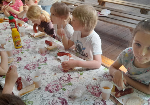 Dzieci siedzą przy stole i jedzą kiełbaski