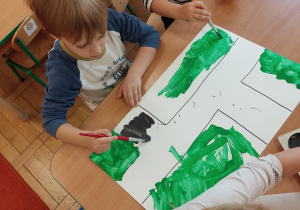 Dzieci siedzą przy stoliku i malują farbami.
