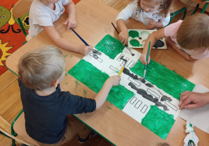 Dzieci malują drogę szarą farbą.