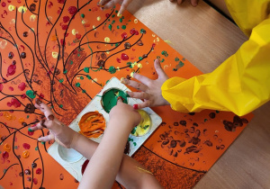 Dzieci malują paluszkami jesienne drzewa.