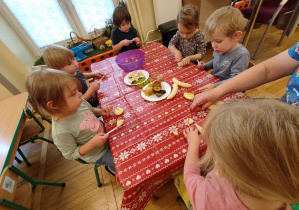 Dzieci przy stole kroją owoce.