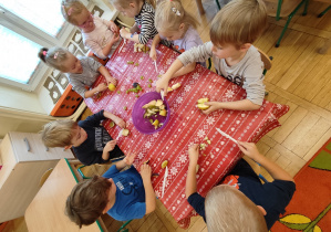 Dzieci kroją owoce i wrzucają do miski.