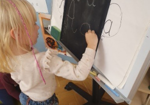 Dziewczynka pisze na tablicy literkę "A"