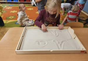 Dziewczynka pisze literkę "A" na tablicy z piaskiem.