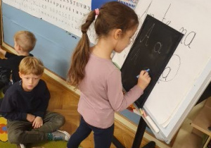 Dziewczynka pisze kredą na tablicy literę "A".