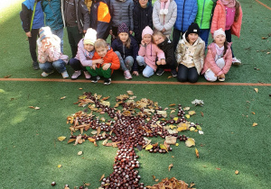 Na zdjęciu widać drzewo ułożone na boisku z darów jesieni. Za nim stoją dzieci, które układały ten obraz.