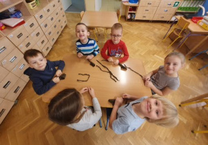 Dzieci z krepiny skręcają długie sznurki, które będą gałązkami dzrewa.