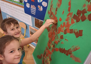 Dzieci malują farbami pień i konary drzewa.