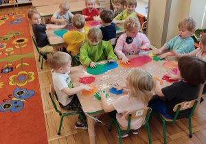 Dzieci bawią się farbą przy stoliku.