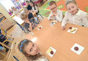 Dzieci siedzą przy stolikach i częstują się ciastem.