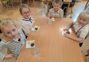 Dzieci siedzą przy stolikach i częstują się ciastem.