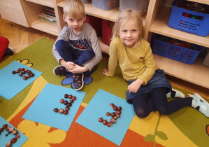 Dzieci układają z kasztanów dużą literkę E